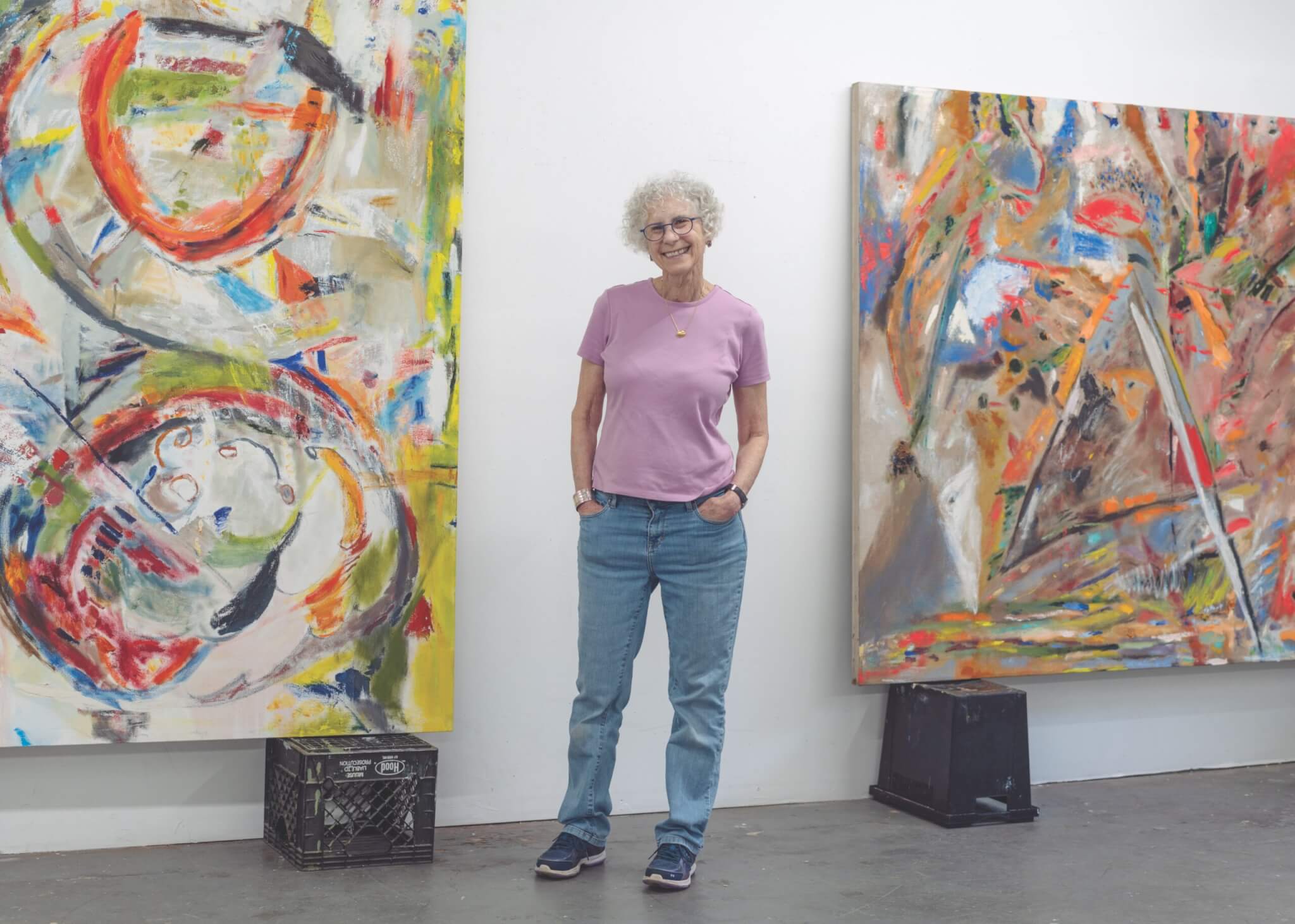 Artist Jo Ann Rothschild stands between two large hung canvases that feature her signature mark making painting technique.